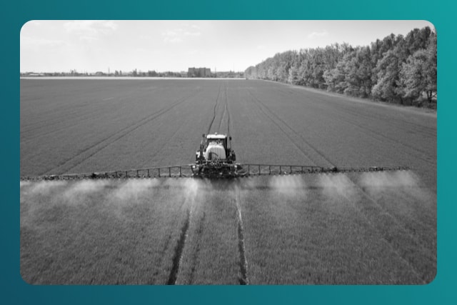 Tractor spraying pesticides with sprayer on the large green agricultural field
